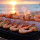 Grilling shrimp and vegetables on a Himalayan salt block at a beachside BBQ with sunset glow