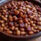 BBQ side dish recipe: Hearty baked beans with bacon and molasses, slow-cooked Kansas City style, with a Texas chili twist, served in a rustic bowl