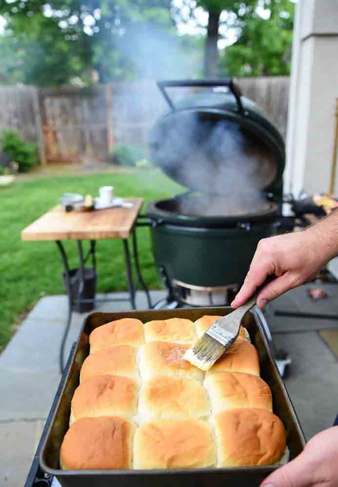 Brushing melted butter on smoked Hawaiian rolls straight off the Big Green Egg - Popular BBQ Brushing melted butter on hot Hawaiian rolls Big Green Egg right after baking for extra soft and shiny tops