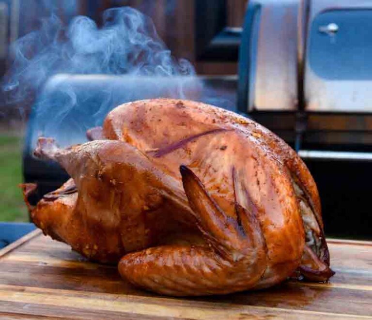 Smoked thanksgiving turkey on offset smoker grate with glowing hickory and cherry wood chunks, thin blue smoke rising, temperature probe in thigh, fire-lit metallic interior, backyard dusk setup