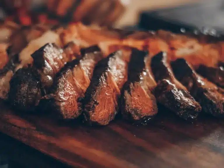 Sliced smoked tri-tip arranged in even pieces on a dark surface, showing the pink interior and dark bark from the reverse sear