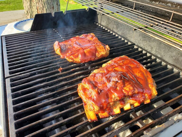 Barbecue grill with glossy glazed pork ribs cooking outdoors in a sunny backyard.