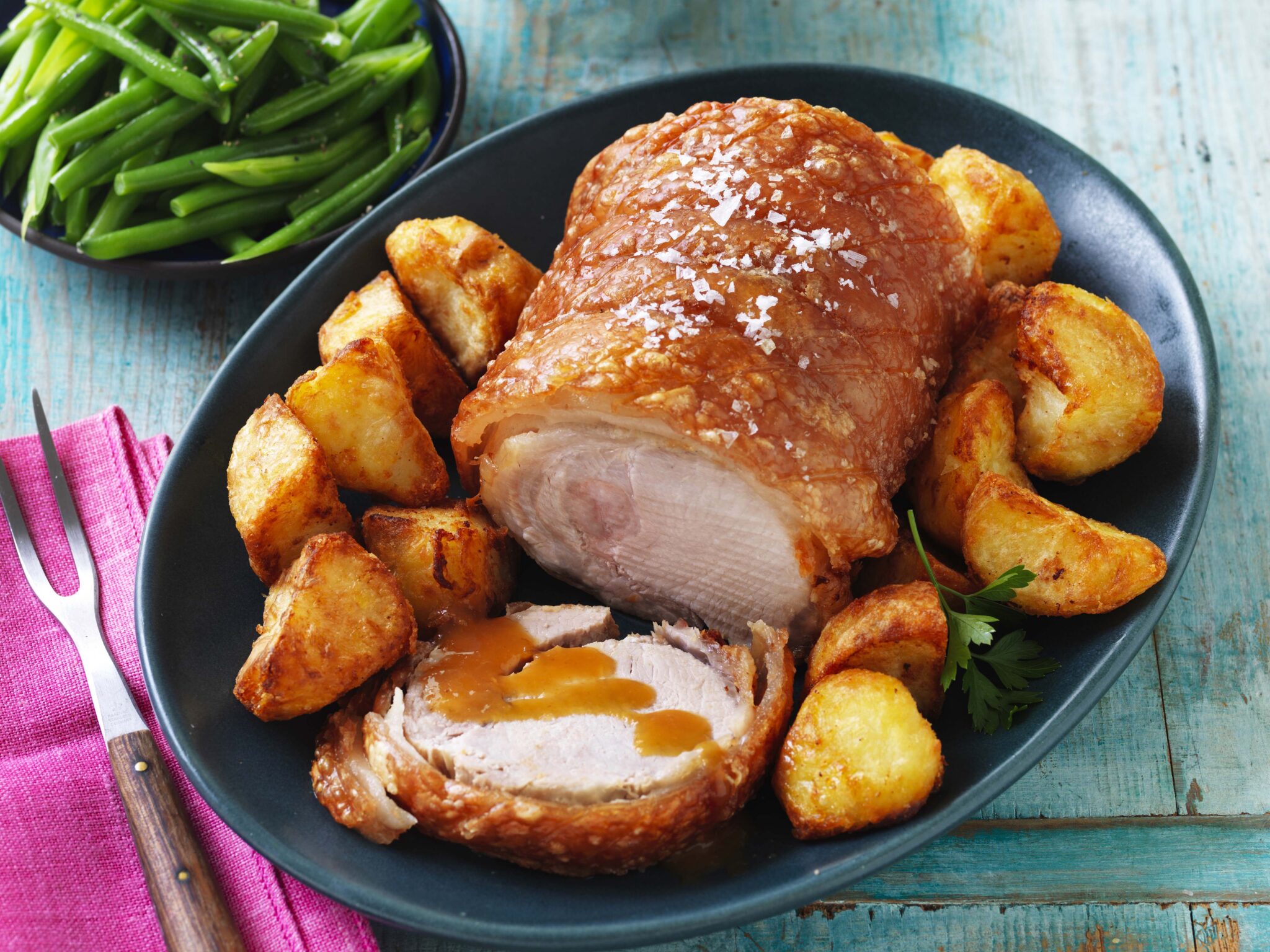 Air-fryer-pork-loin-roast_main - Popular BBQ Roasted chicken with crispy skin and potatoes on a dark plate, served with green beans on the side.