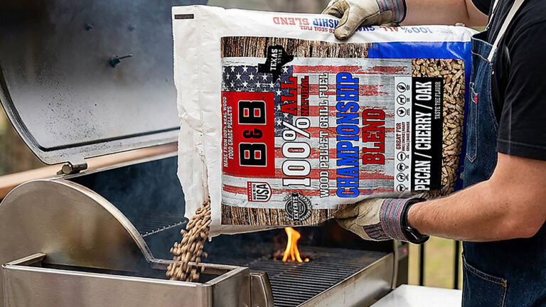 A person wearing gloves pours a bag of wood pellets into a barbecue grill for cooking.