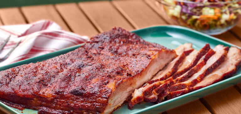 Barbecued pork ribs sliced on a green serving platter with a wooden table background