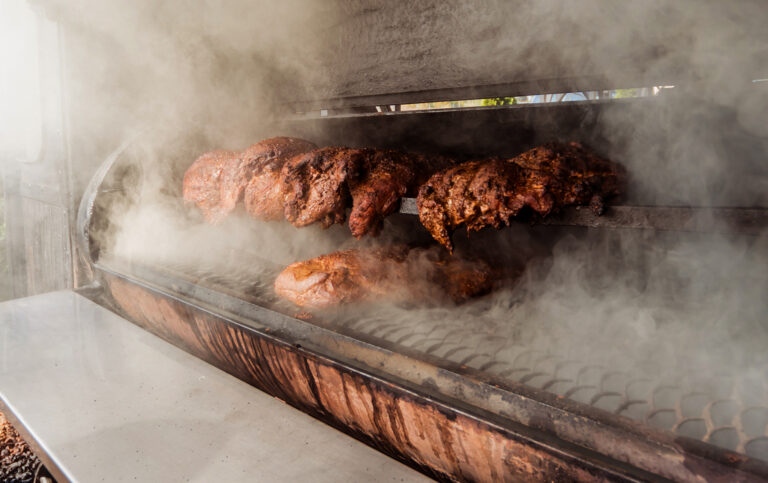 Racks of smoked barbecue ribs cooking inside a smoker with thick steam rising around them to a smoky scene is depicted here?