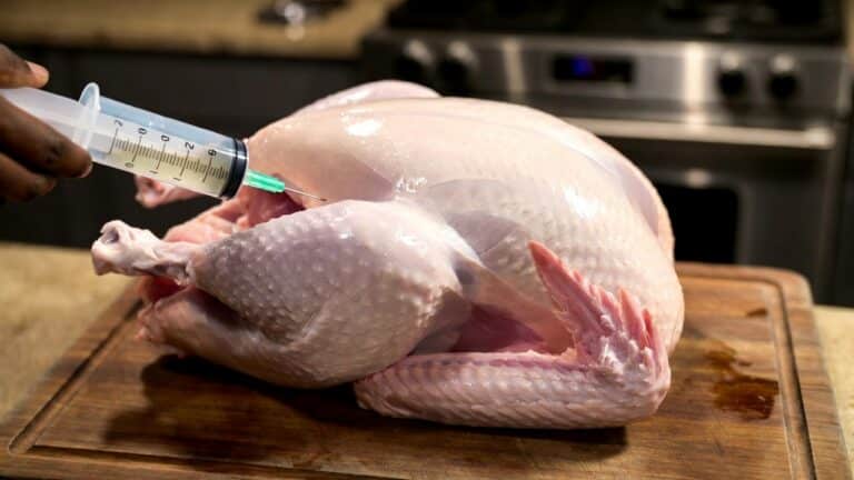 Raw whole turkey on a cutting board being injected with a syringe in a home kitchen, preparing for brining or stuffing the meat