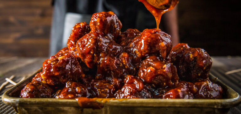 Pile of glossy barbecue meatballs coated in thick sauce on a baking tray